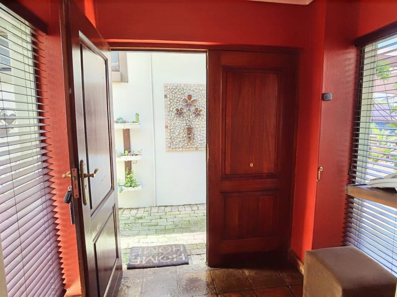 Entrance area featuring timber doors, tiled flooring, and venetian blinds, opening out to a paved courtyard with a decorative wall mosaic.