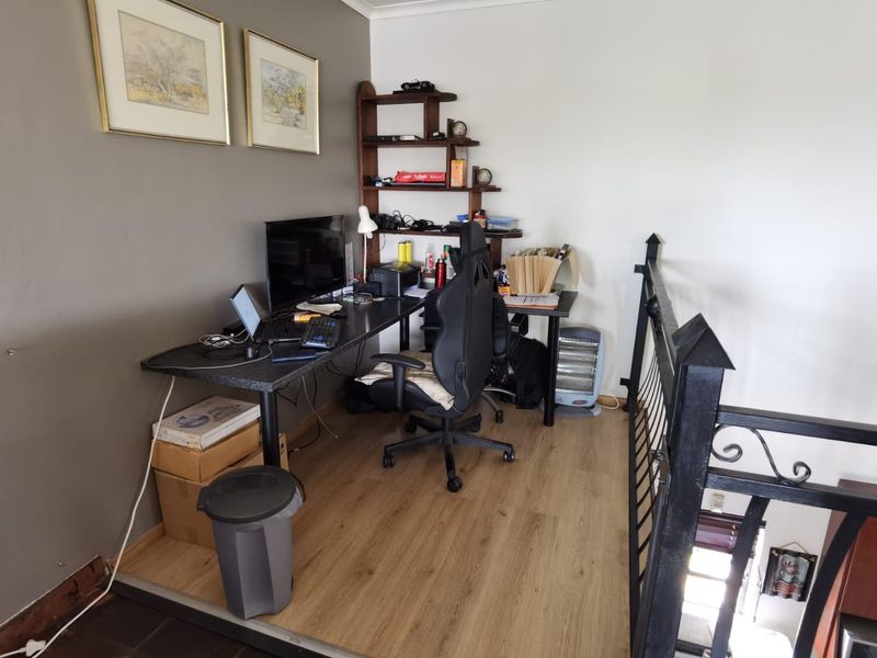 A functional home office space featuring laminate flooring and a decorative wrought iron balustrade overlooking the lower level.