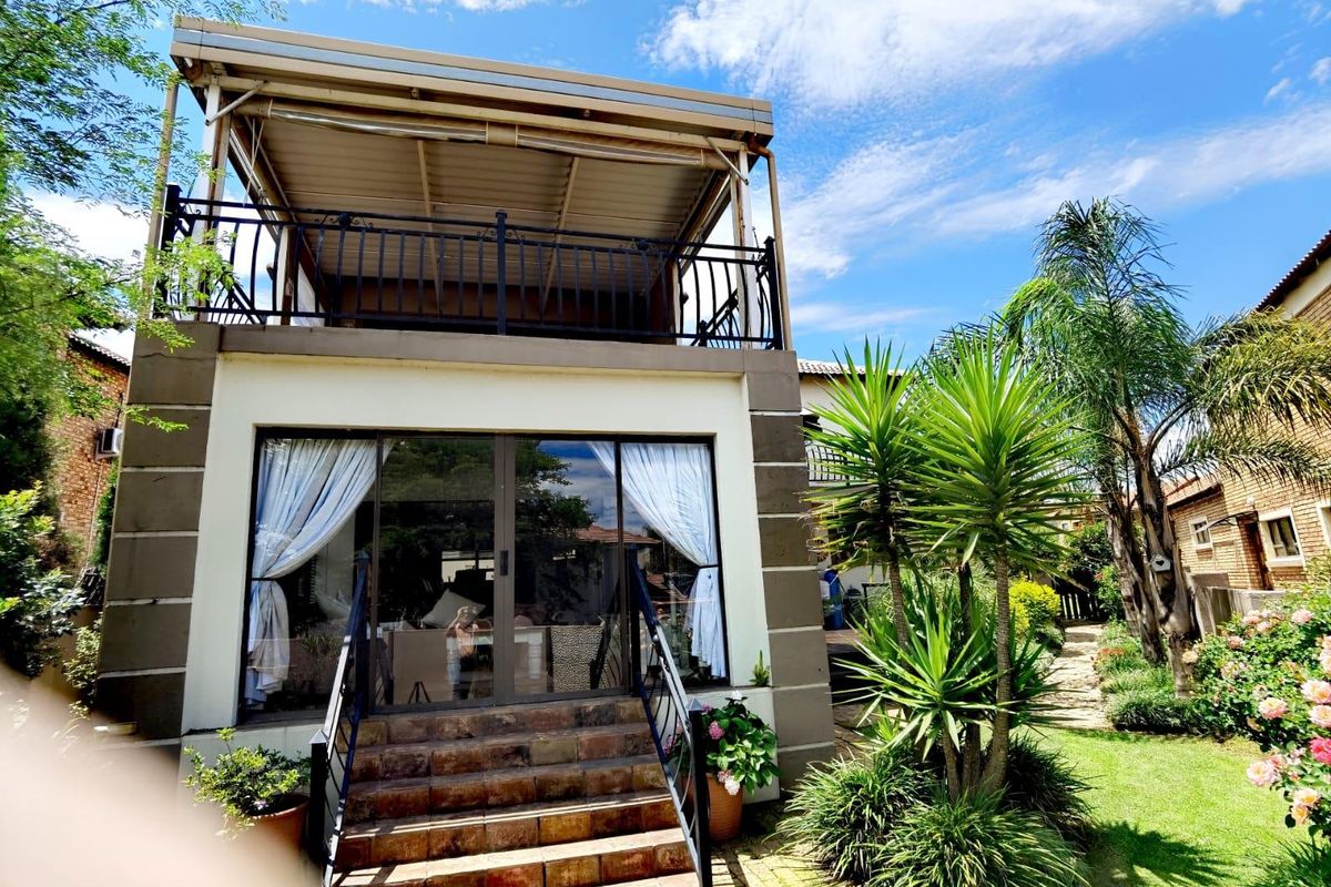 Rear view of the property featuring a covered upper balcony, sliding glass doors leading to the interior, and a well-maintained garden with tiled stairs.