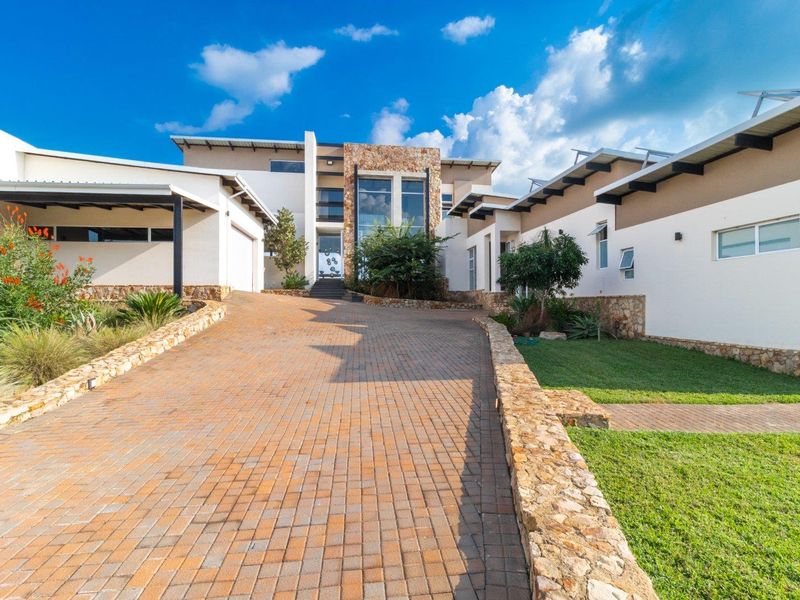 A modern residential property featuring a paved driveway, stone-clad facade, and well-maintained landscaped gardens leading to the main entrance.