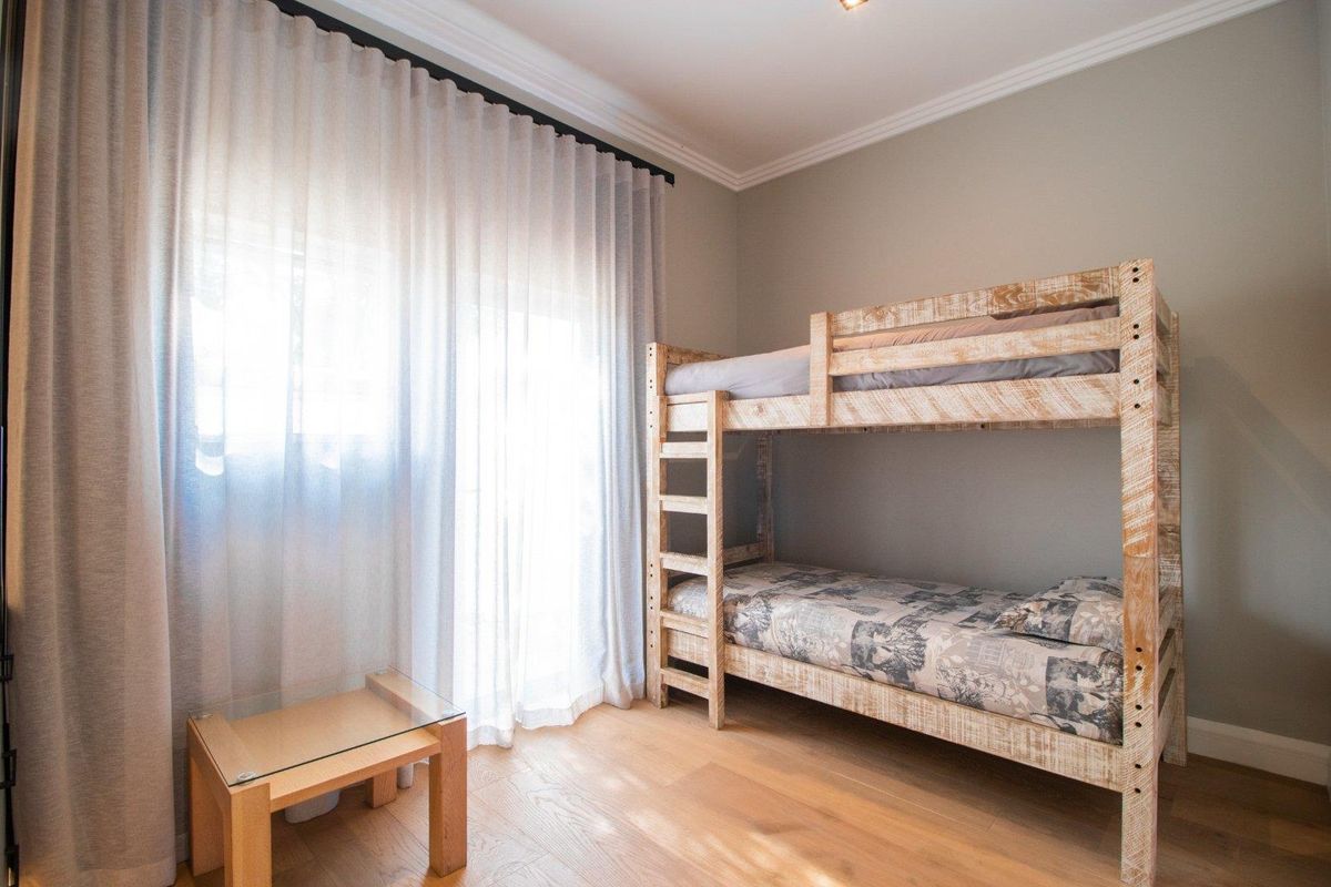 A well-maintained bedroom featuring timber flooring, neutral wall tones, and a sliding door with sheer curtains providing natural light.