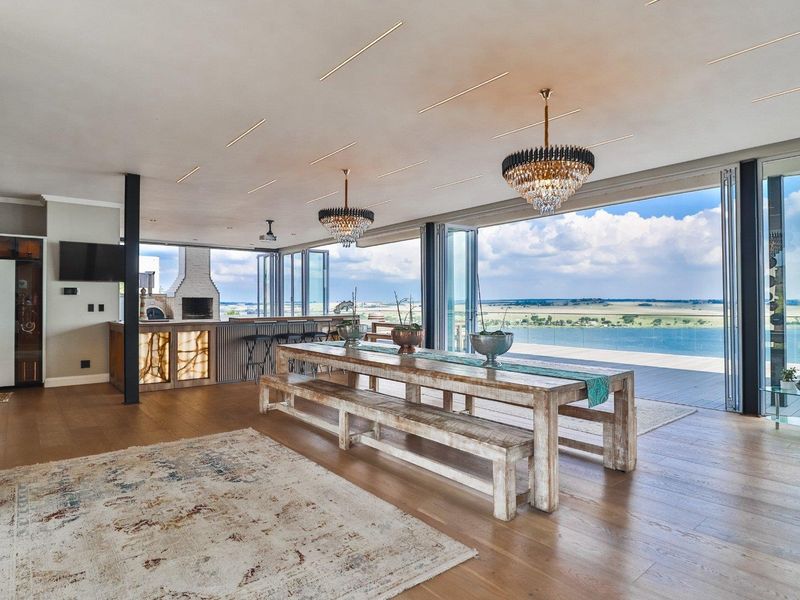 Spacious open-plan living and dining area featuring a built-in bar, fireplace, and expansive stacking glass doors opening to a scenic waterfront view.