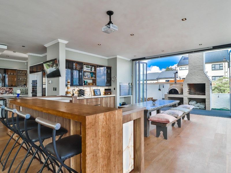 Spacious open-plan living area featuring a modern kitchen with stone countertops, seamless indoor-outdoor flow through bi-fold doors to a patio with a brick fireplace.