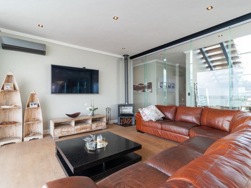 Modern living room featuring hardwood flooring, a sleek wood-burning fireplace, recessed lighting, and a contemporary glass partition wall overlooking the staircase.