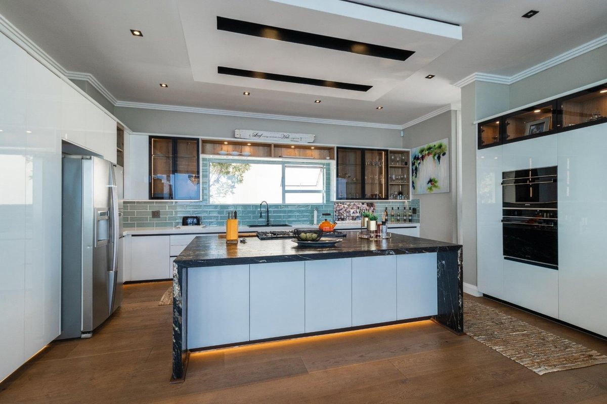 Modern kitchen featuring a large stone-topped island, high-end built-in appliances, subway tile backsplash, and elegant recessed ceiling lighting with warm under-cabinet accents.
