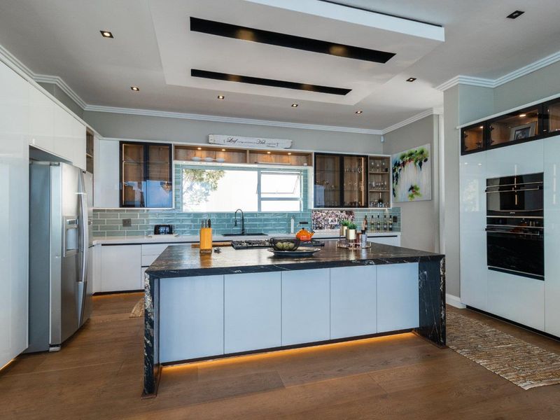 Modern kitchen featuring a large stone-topped island, high-end built-in appliances, subway tile backsplash, and elegant recessed ceiling lighting with warm under-cabinet accents.