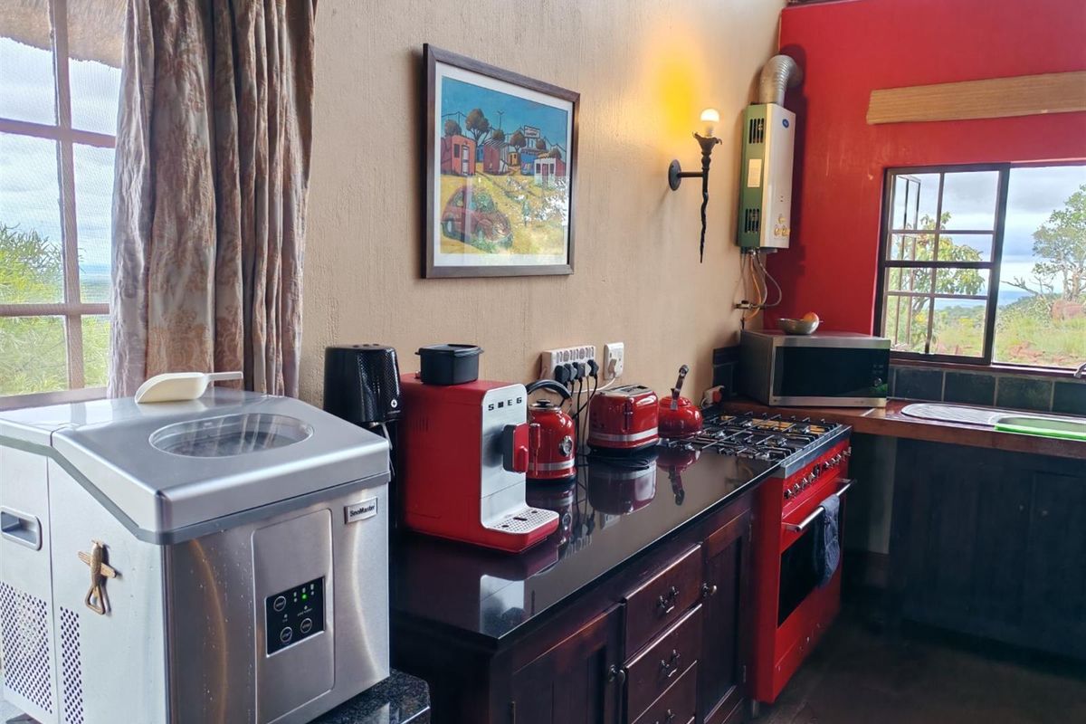 A rustic kitchen featuring dark wood cabinetry, black granite countertops, a red gas stove, and a wall-mounted gas geyser.