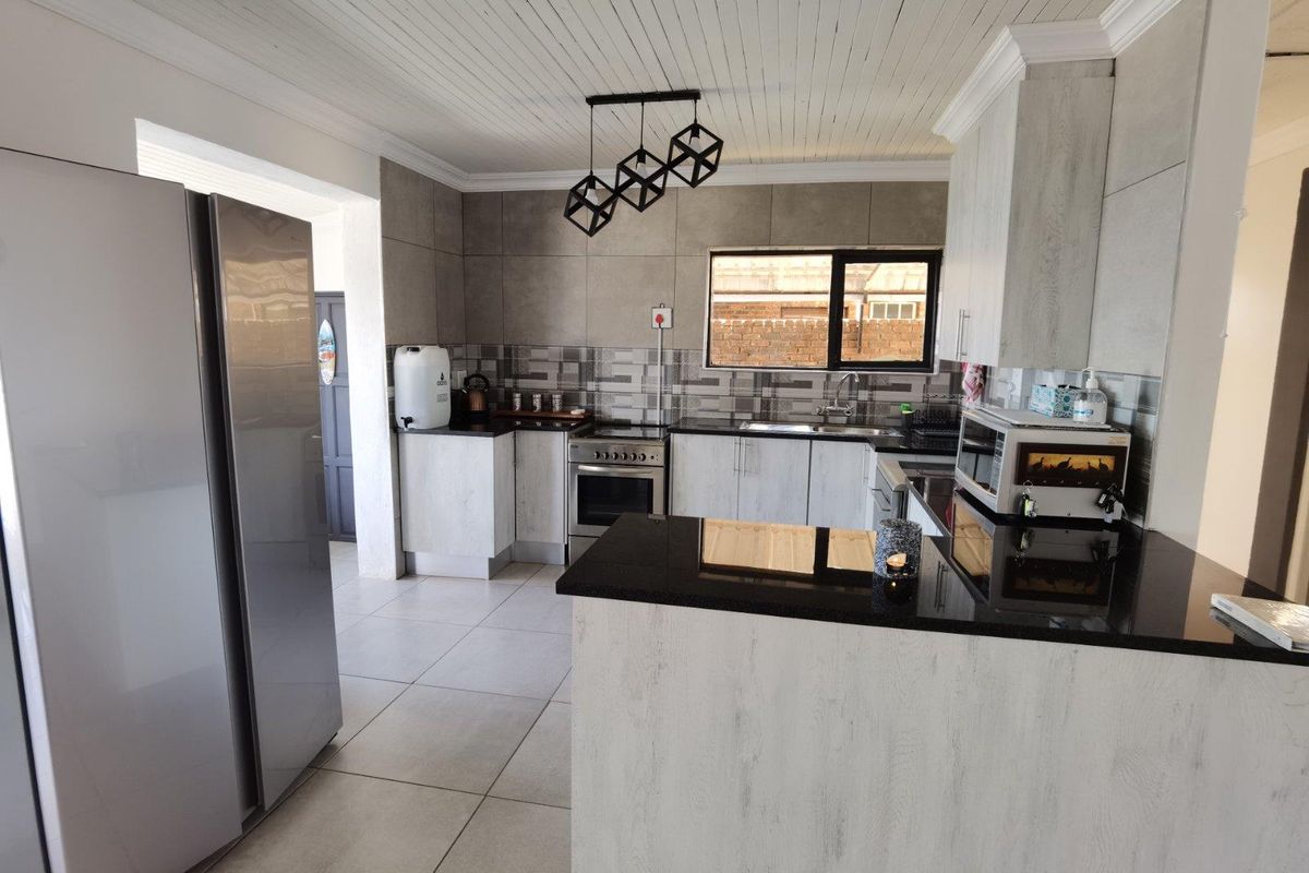 Modern kitchen featuring light wood-grain cabinetry, sleek black granite countertops, stainless steel appliances, and a functional breakfast nook layout.