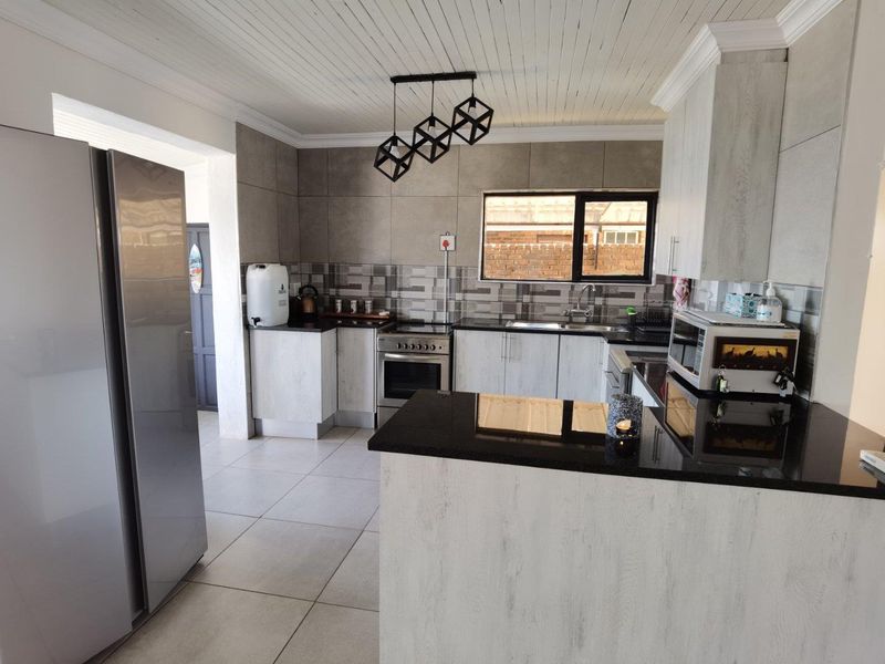 Modern kitchen featuring light wood-grain cabinetry, sleek black granite countertops, stainless steel appliances, and a functional breakfast nook layout.