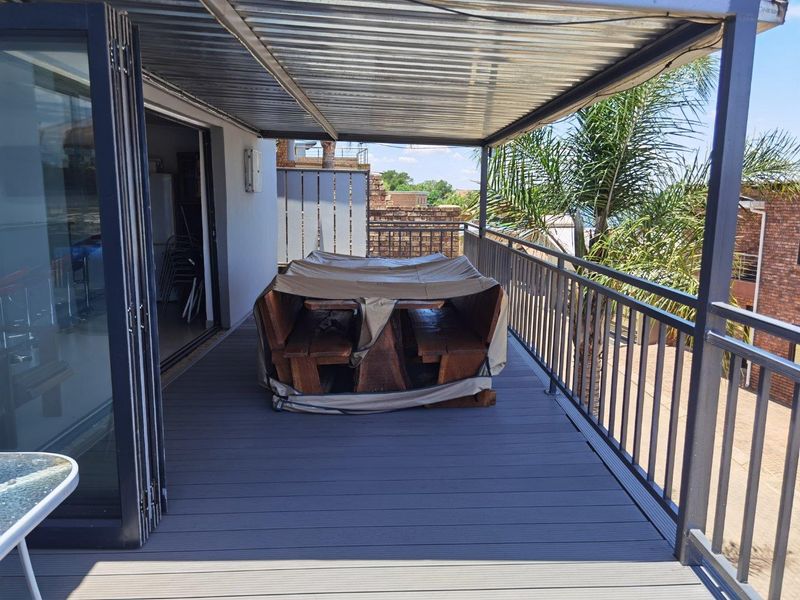 A covered balcony featuring composite decking, metal railings, and folding glass doors, providing a functional outdoor entertainment space.