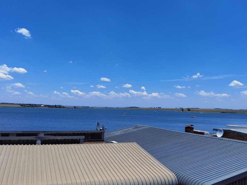Elevated view overlooking a large lake, featuring corrugated metal roofing and a brick chimney in the foreground.