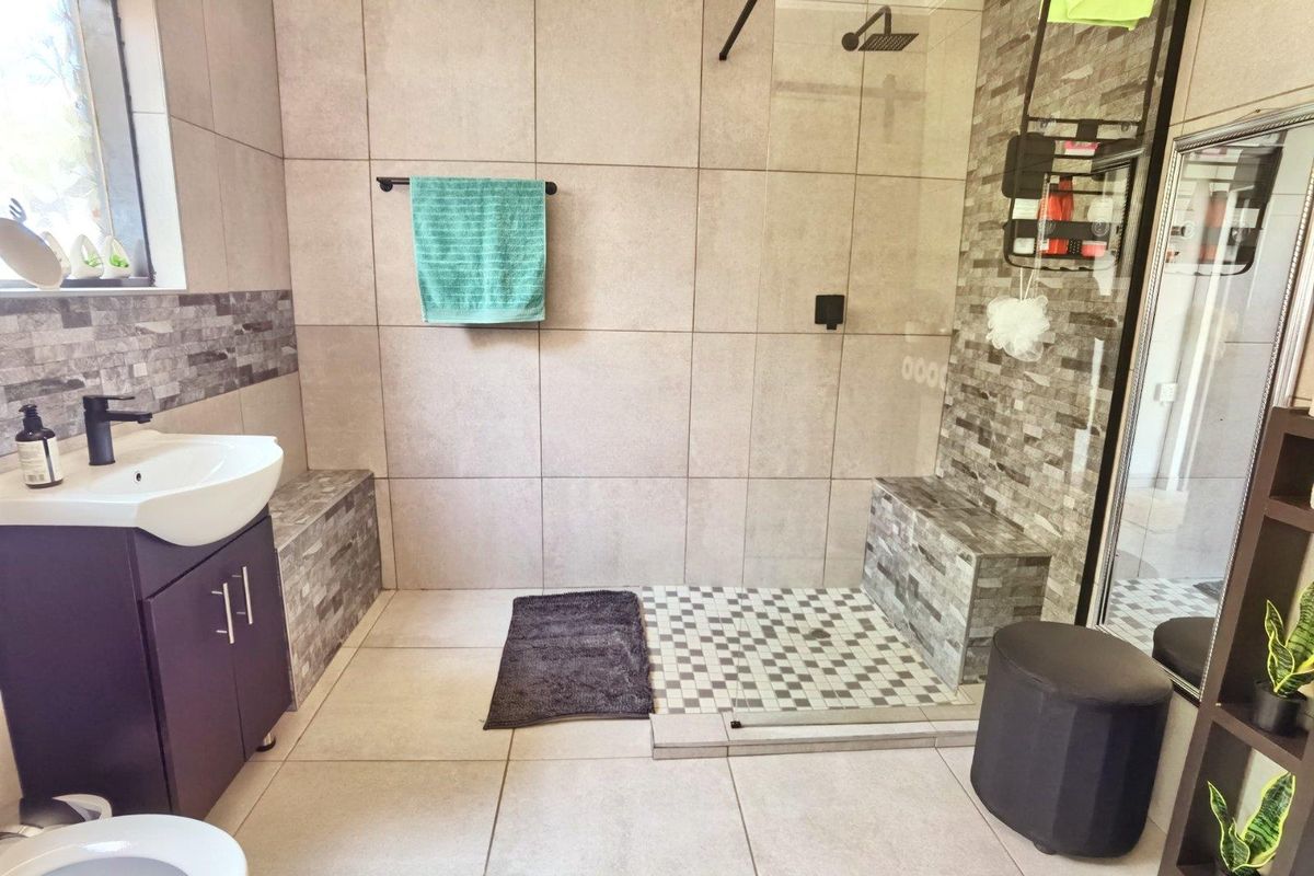 Modern bathroom featuring a spacious walk-in shower with a glass screen, tiled bench, and a contemporary vanity unit with a basin.
