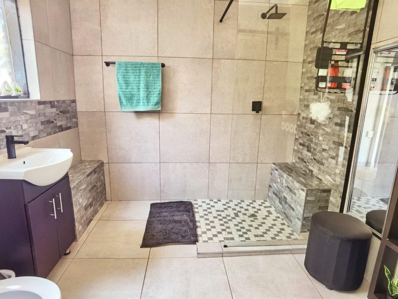 Modern bathroom featuring a spacious walk-in shower with a glass screen, tiled bench, and a contemporary vanity unit with a basin.