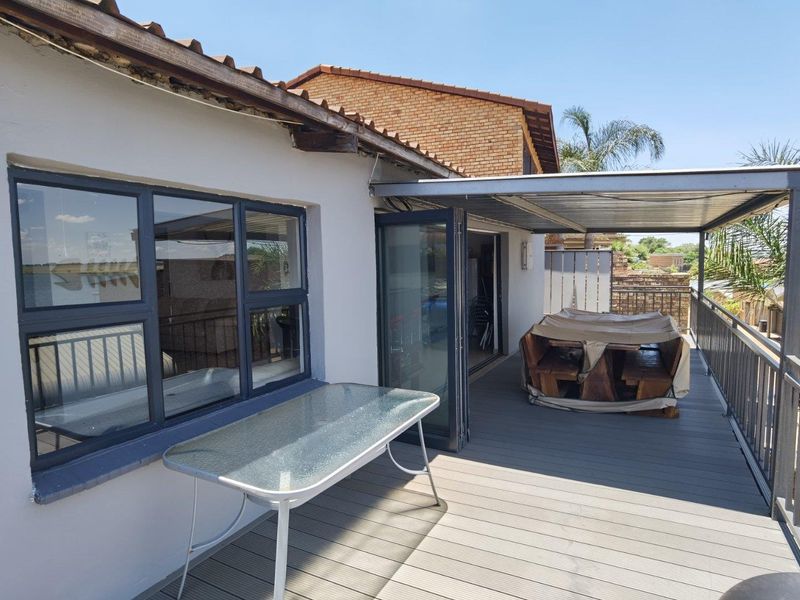 An elevated balcony featuring composite decking, a covered metal roof structure, and folding glass doors providing access to the interior living space.