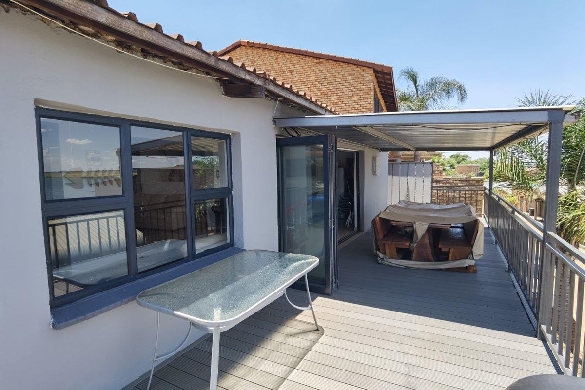 An elevated balcony featuring composite decking, a covered metal roof structure, and folding glass doors providing access to the interior living space.