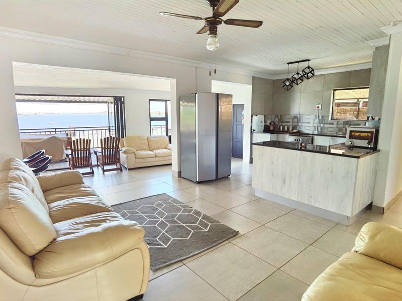 Spacious open-plan living and kitchen area featuring tiled floors, a central island with granite countertops, and direct access to a balcony with water views.