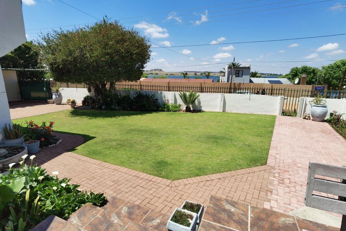 A well-maintained rear garden featuring a manicured lawn, paved walkways, and perimeter walling with metal fencing, offering a pleasant outdoor space.