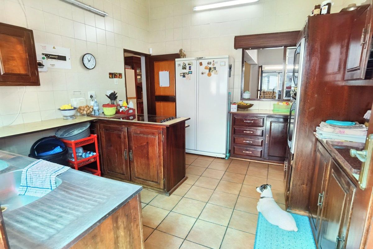 A dated kitchen featuring traditional wooden cabinetry, tiled walls, and a functional layout with a serving hatch to the adjacent living area.