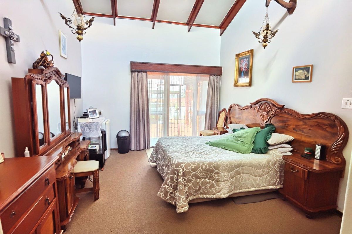 Spacious bedroom featuring high vaulted ceilings with exposed timber beams, carpeted flooring, and sliding glass doors providing access to the outdoor area.