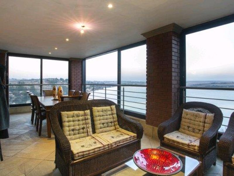 A spacious covered patio featuring exposed brick columns, tiled flooring, and a stainless steel balustrade, offering expansive views through large sliding glass doors.
