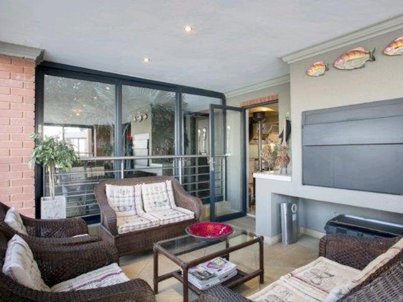 Covered patio featuring a built-in braai, tiled flooring, and large sliding glass doors providing seamless access to the interior living space.