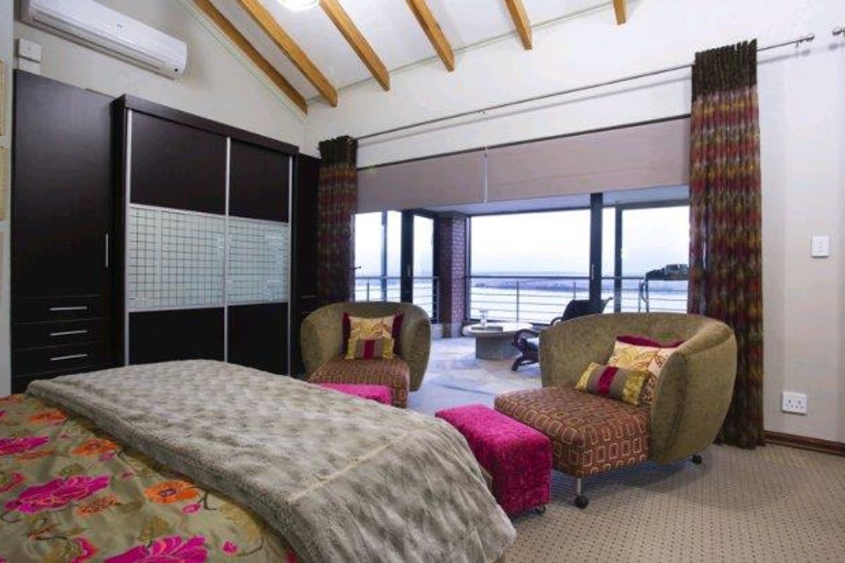 Spacious bedroom featuring exposed timber rafters, built-in cupboards, and large sliding glass doors opening onto a private balcony with scenic views.