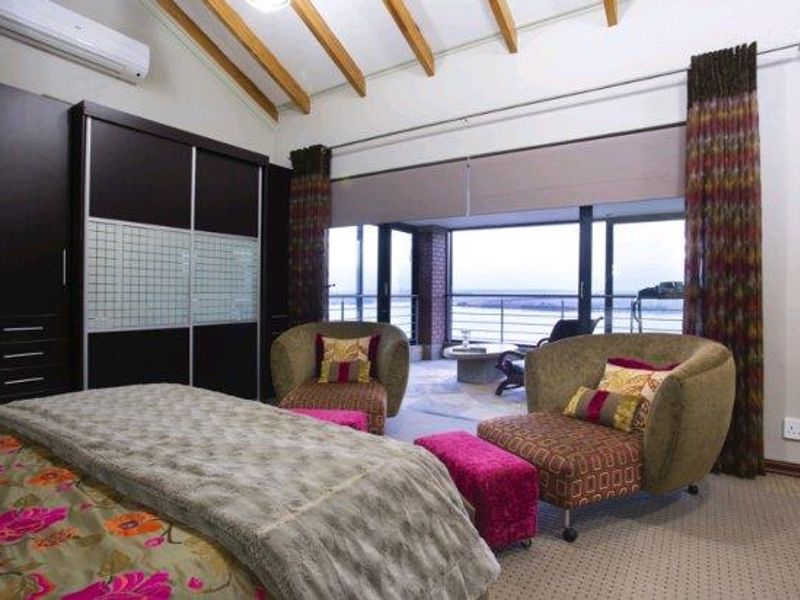 Spacious bedroom featuring exposed timber rafters, built-in cupboards, and large sliding glass doors opening onto a private balcony with scenic views.