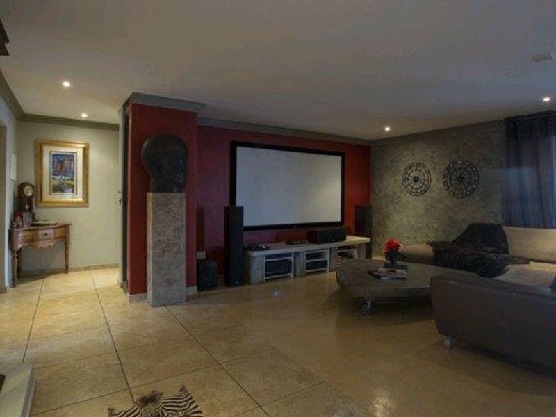 A dedicated cinema room featuring a large built-in projection screen, recessed downlighting, and tiled flooring with a distinct feature wall.