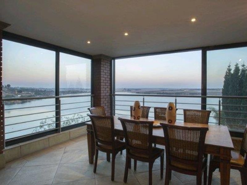 Covered balcony featuring tiled flooring, exposed brick accents, and stainless steel balustrades, offering expansive views of the water.