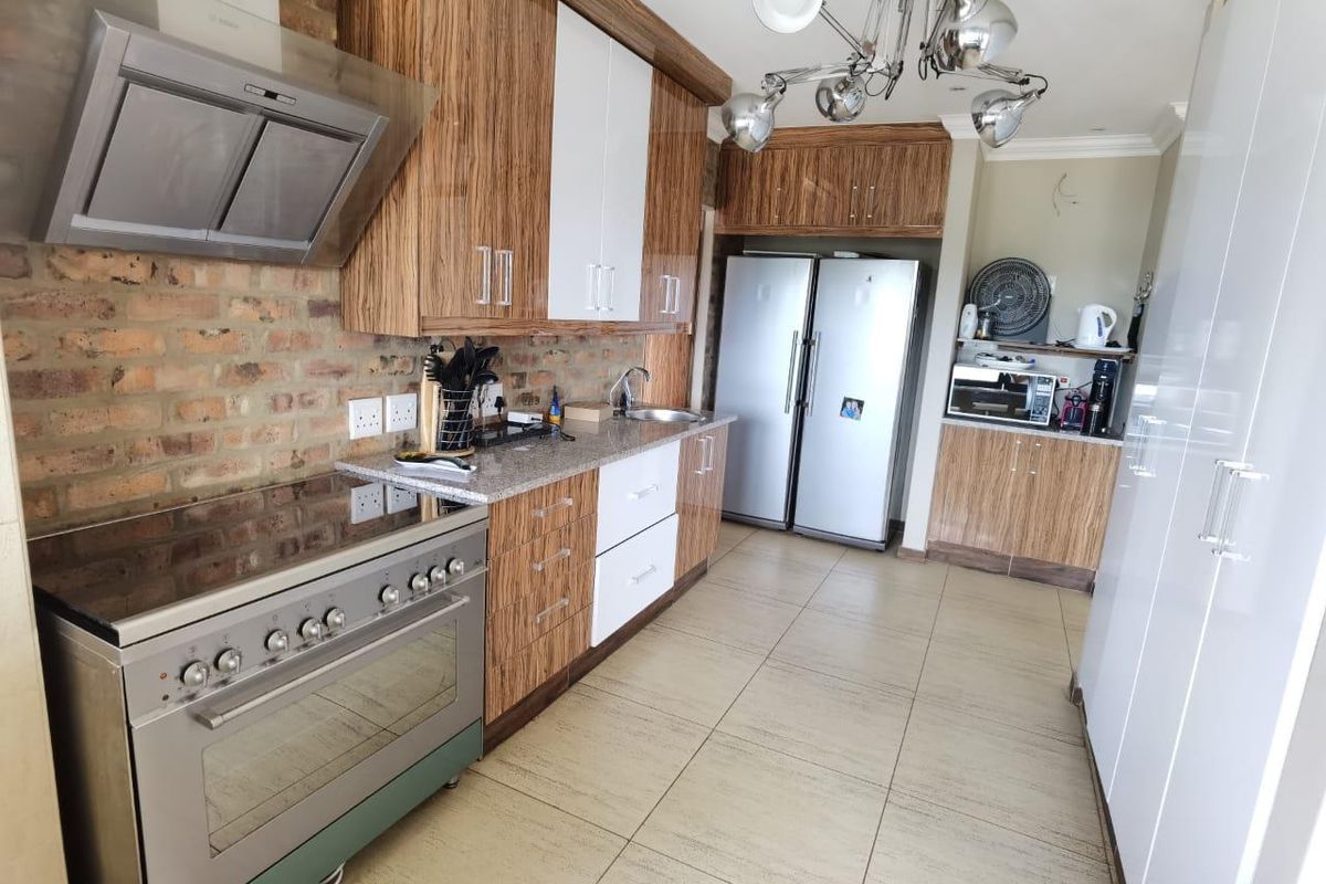 Modern kitchen featuring wood-grain cabinetry, granite countertops, exposed brick backsplash, stainless steel oven, and extractor fan with tiled flooring.
