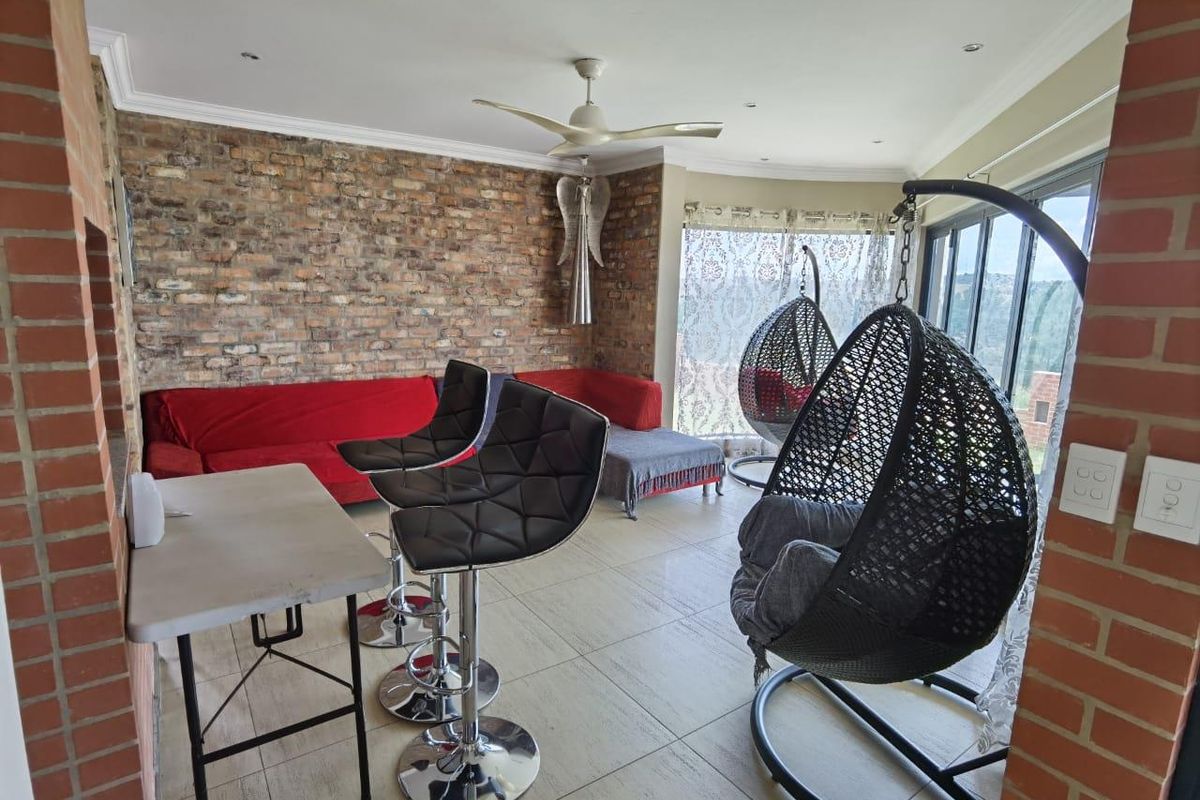 A living area featuring an exposed brick feature wall, tiled flooring, a ceiling fan, and large sliding doors leading to an outdoor space.