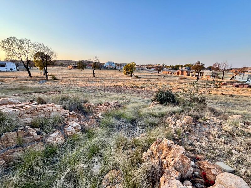 A wide-angle view of the vacant residential land, featuring natural rock outcrops and native vegetation with surrounding neighborhood development in the distance.
