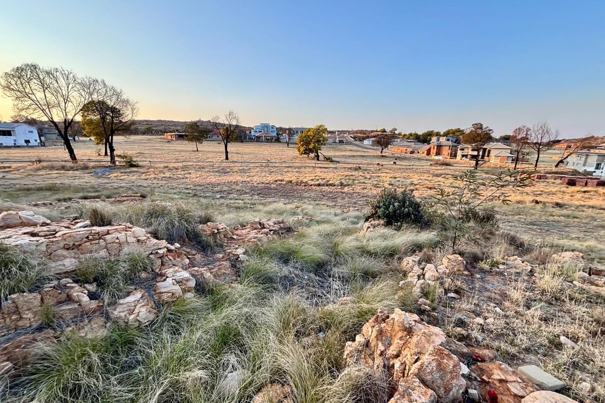 A wide-angle view of the vacant residential land, featuring natural rock outcrops and native vegetation with surrounding neighborhood development in the distance.
