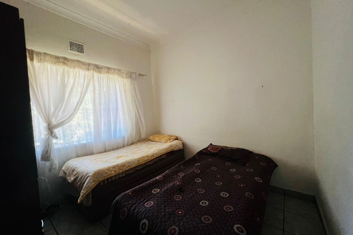 A functional bedroom featuring tiled flooring, a large window with curtain rod, and integrated wall ventilation.