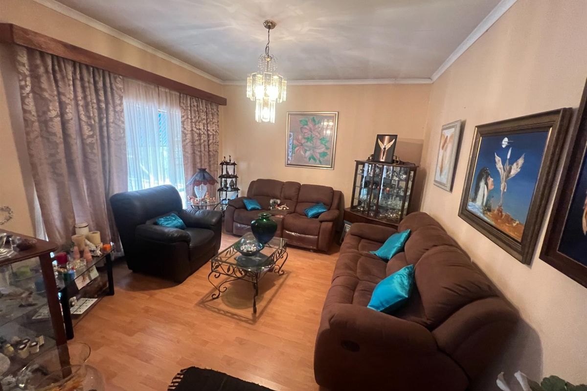 A comfortable living room featuring laminate flooring, a central chandelier, and large windows with curtain pelmets.