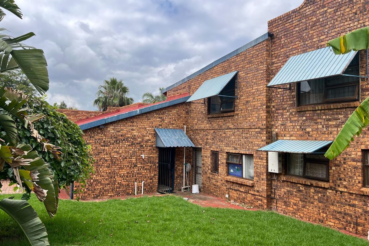 Rear view of a face-brick residential property featuring metal window awnings, a small paved area, and a surrounding lawn.