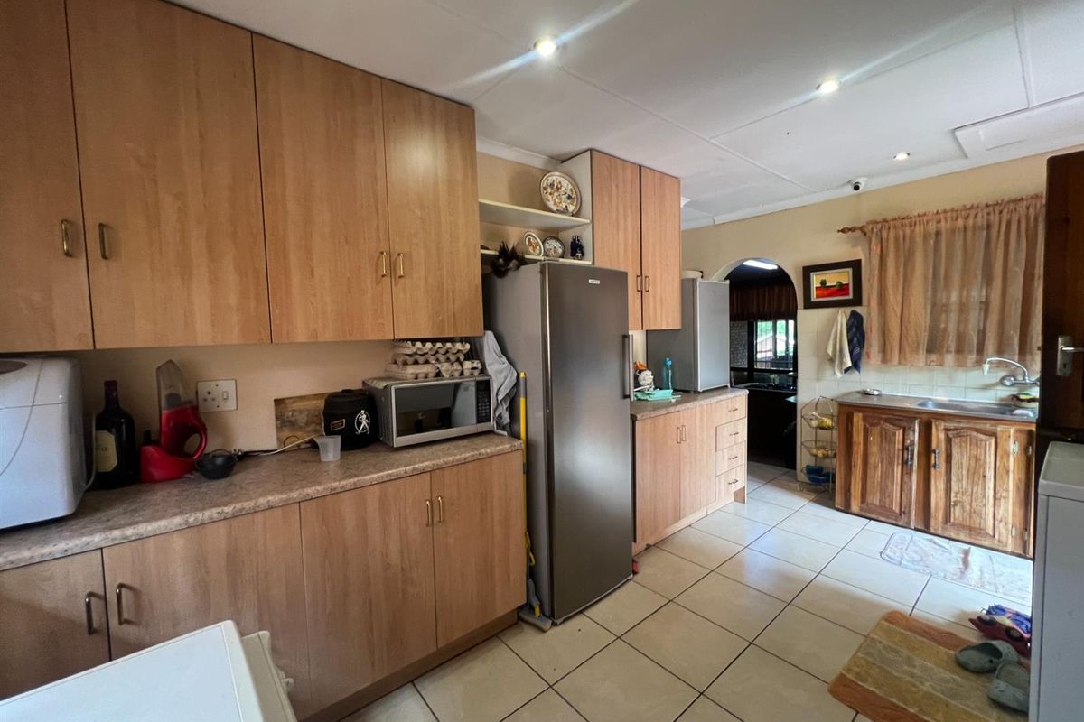 A functional kitchen featuring wood-look laminate cabinetry, tiled flooring, and recessed ceiling lighting, offering a practical layout with ample storage space.