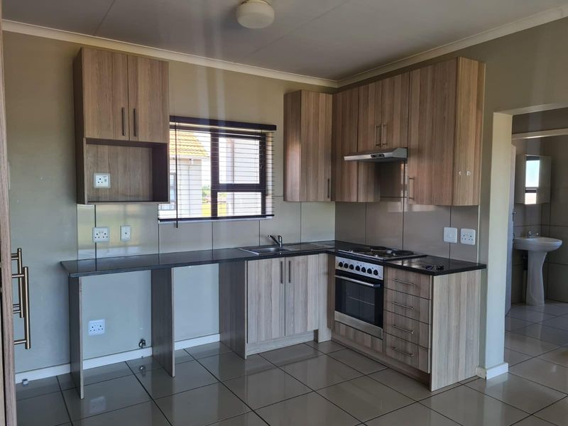 Modern kitchen featuring light wood-grain cabinetry, dark countertops, built-in oven with gas hob, extractor fan, and tiled flooring.