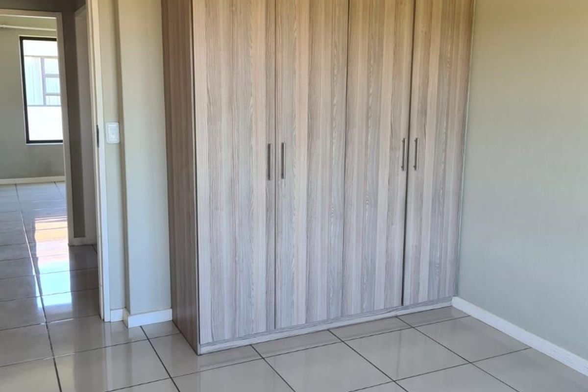 A clean, empty bedroom featuring light-toned built-in wardrobes and neutral tiled flooring, offering a versatile space ready for personalization.