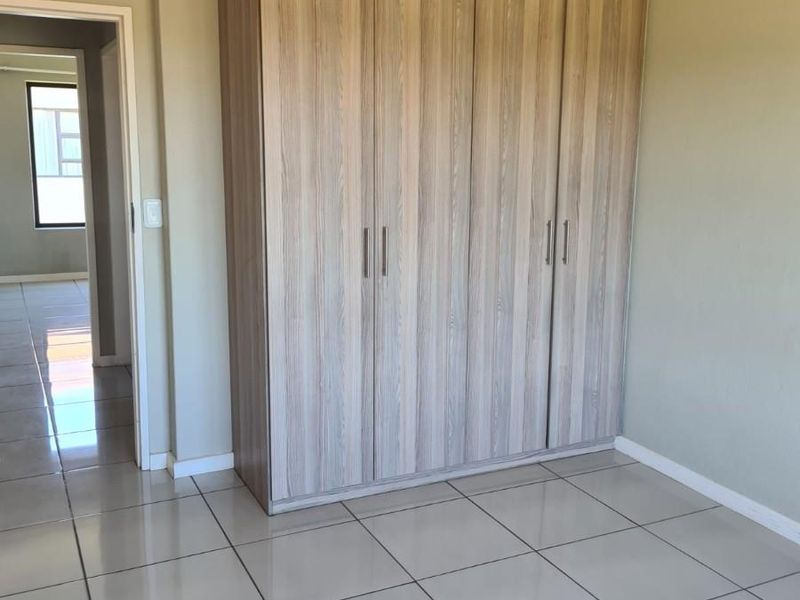 A clean, empty bedroom featuring light-toned built-in wardrobes and neutral tiled flooring, offering a versatile space ready for personalization.