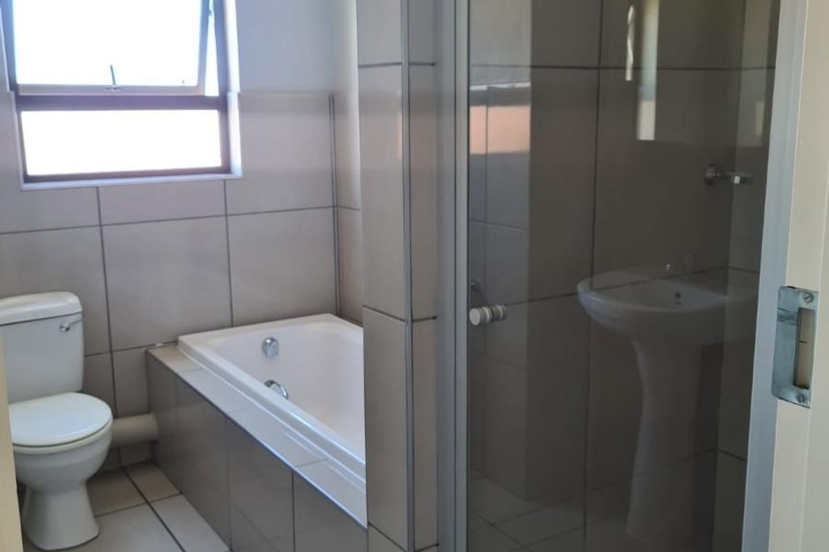 A clean, modern bathroom featuring a built-in bathtub, a separate glass-enclosed shower, and a pedestal basin with neutral wall and floor tiling.