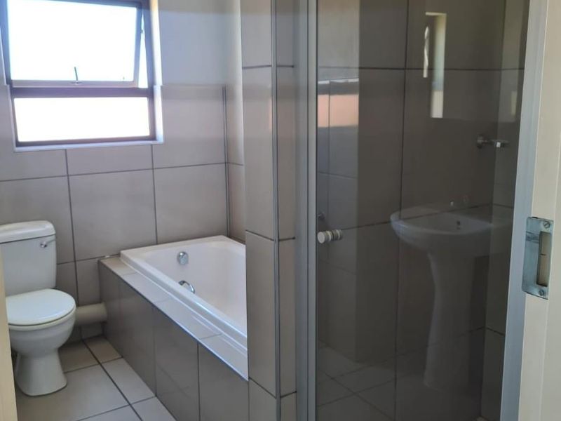 A clean, modern bathroom featuring a built-in bathtub, a separate glass-enclosed shower, and a pedestal basin with neutral wall and floor tiling.