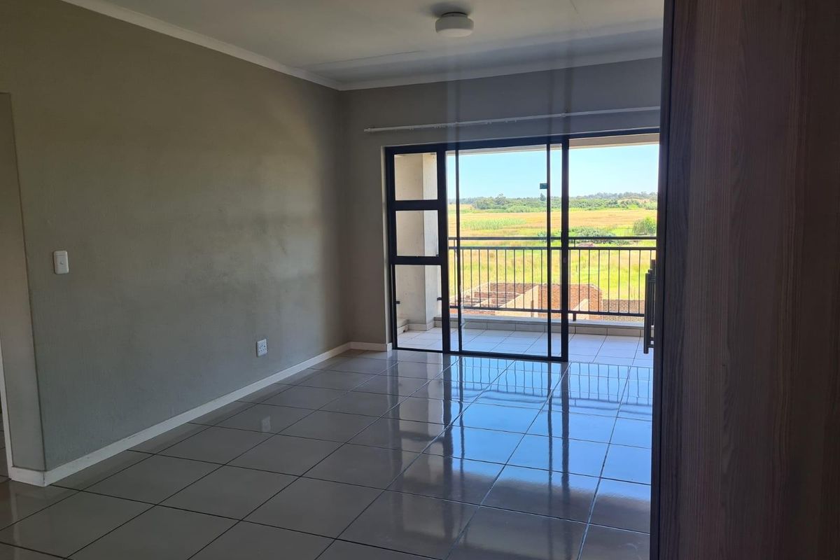 An empty, well-lit living area featuring neutral tiled floors and a large sliding glass door providing access to a balcony with scenic views.