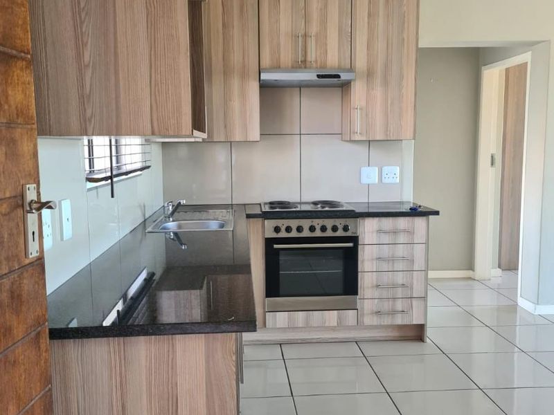 Modern kitchen featuring wood-look laminate cabinetry, granite countertops, built-in oven with electric hob, extractor fan, and neutral tiled flooring.