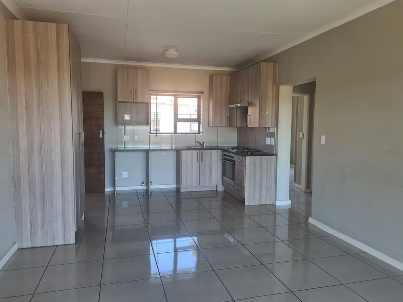 A modern, open-plan kitchen featuring light wood-grain cabinetry, tiled flooring, built-in oven and hob, and ample counter space in a clean, vacant setting.