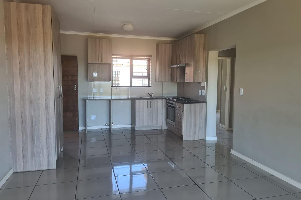 A modern, open-plan kitchen featuring light wood-grain cabinetry, tiled flooring, built-in oven and hob, and ample counter space in a clean, vacant setting.