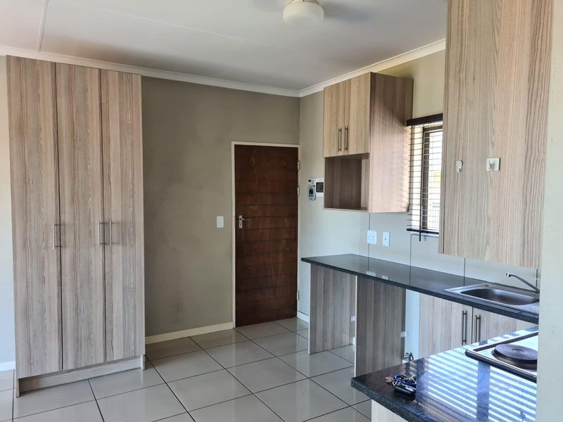 A clean, modern kitchen featuring light wood-grain cabinetry, dark laminate countertops, tiled flooring, and a built-in hob, offering a functional and well-maintained workspace.