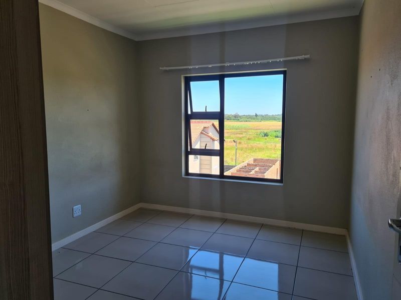 A bright, empty bedroom featuring neutral walls, tiled flooring, and a large window with a view of the surrounding landscape.
