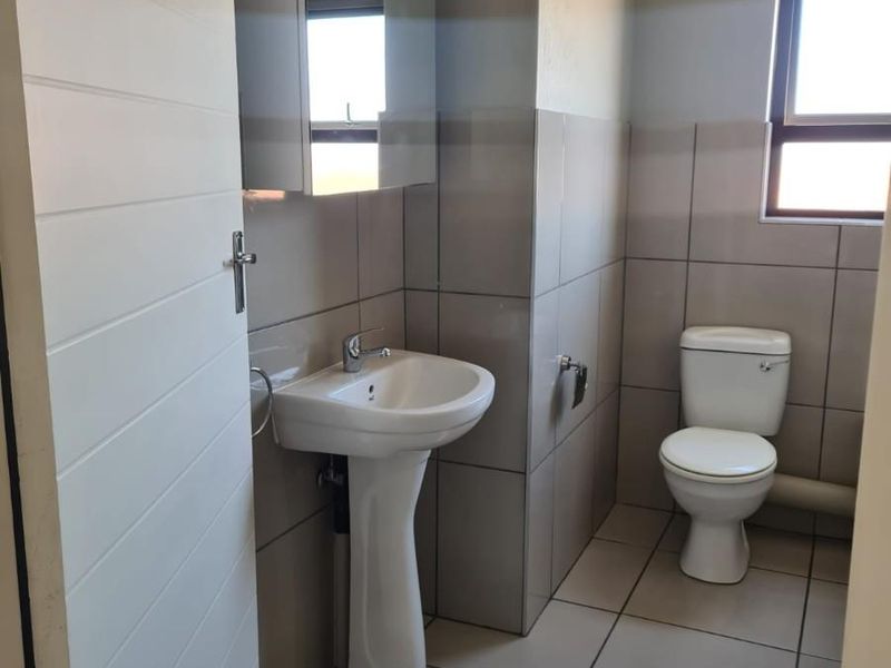 A clean, functional bathroom featuring a pedestal sink, a mirrored medicine cabinet, a standard toilet, and neutral ceramic wall and floor tiling.