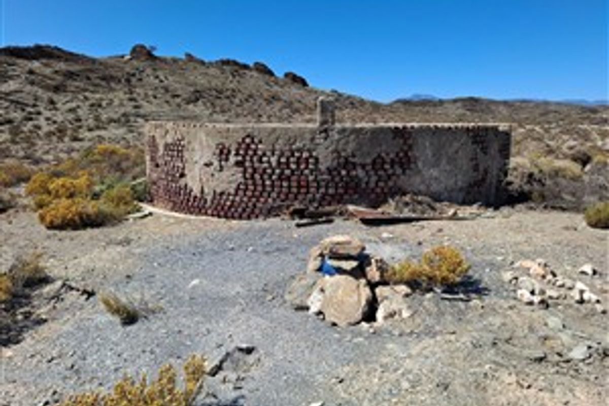 An old, weathered stone water reservoir structure located in a rural farm landscape, showing significant signs of age and material deterioration.
